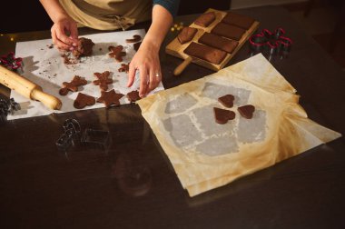 Ellerin parşömen üzerinde zencefilli kurabiye şekillendirdiği ve kestiği sıcak mutfak sahnesi, merdane ve fırın tepsisiyle. Şenlikli şekiller sıcak bir Noel anı oluşturur. Pişirme ve aile birlikteliği..