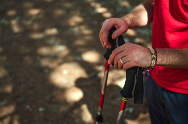 Yürüyüşçülerin, güneşli bir ormanda yürüyüş direkleri üzerinde kırmızı bir gömlek ve bilezik takıp, açık hava yürüyüşüne hazırlandıkları yakın bir görüntü..