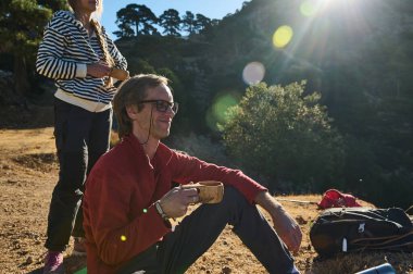 İki arkadaş yürüyüş sırasında güneşli bir yamaçta durup sıcak bir içki içerken sırt çantası yakınlarda oturur, rahat doğa ve açık hava maceralarını yakalar..