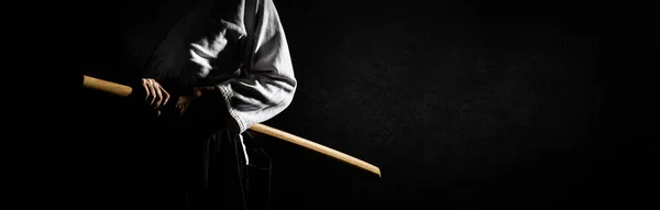 A person in black hakama standing in fighting pose with wooden sword bokken over grunge dark background banner. Shallow depth of field. SDF.