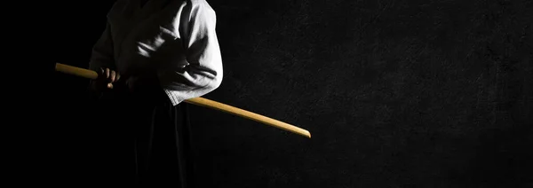 A person in black hakama standing in fighting pose with wooden sword bokken over grungy dark background banner. Shallow depth of field. SDF.