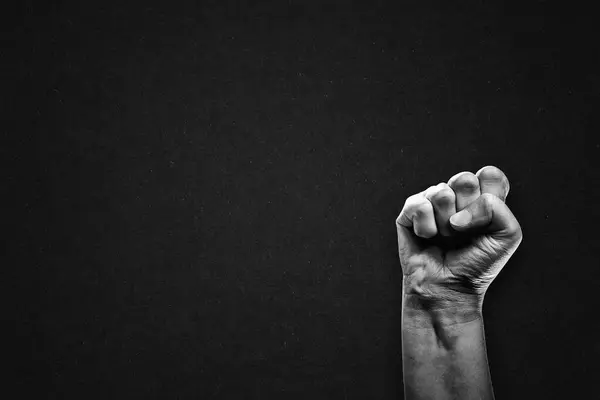Raised Hand Clenched into Fist Symbol Gesture Sign in Black and White on Textured Paper Background, Copy Space