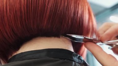 Kuaför kırmızı kısa saçlı bir müşteriye boyun kesimi yapıyor.