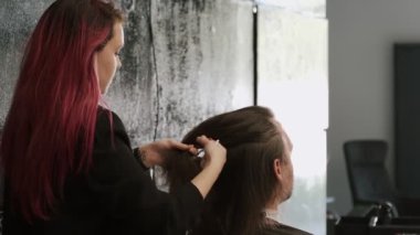 Parlak kızıl saçlı stilist, kuaförde bir erkek müşterinin saçını şekillendiriyor.