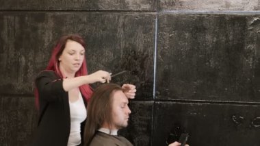 Bir kuaförde erkek müşterinin saçını kesmeye odaklanmış kızıl saçlı bir stilist.