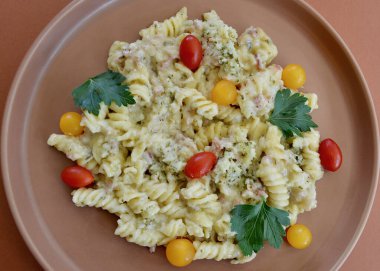 Carbonara makarnası küçük domateslerle pişirilir ve maydanoz yapraklarıyla süslenir.