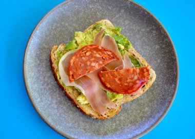 Kızarmış çoklu tahıllı ekmek, parçalanmış avokado ve sıcak salam.