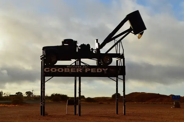 stock image A sign welcoming visitors to Coober Pedy featuring a sand bucket truck used in opal mining.