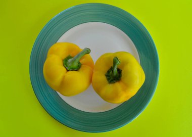 Bir tabakta iki sarı dolma biber renkli bir arka planda. 