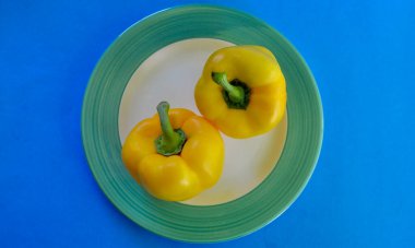 Bir tabakta iki sarı dolma biber renkli bir arka planda. 