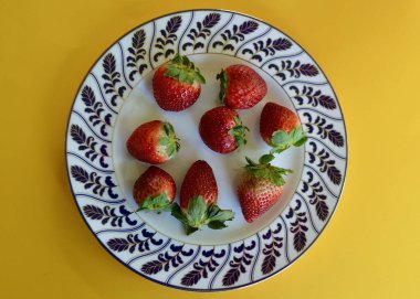 Sarı arka planda dilimlenmiş çilekli tabak.