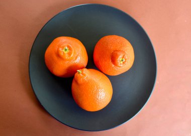 Siyah bir tabakta üç sulu tangelo.