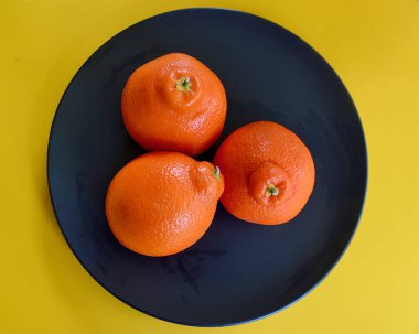 Siyah bir tabakta üç sulu tangelo.