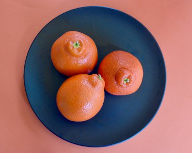 Siyah bir tabakta üç sulu tangelo.