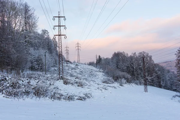 The overhead electric line over blue sky. Electrical wires of power line or electrical transmission line covered by snow in the winter forest.