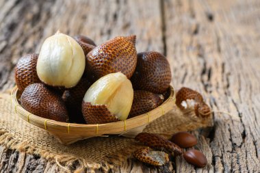 Salak (Salacca zalacca) or Snake fruits on bamboo basket and on old wood background, fruits concept clipart