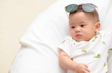 Küçük tatlı Asyalı çocuk beyaz battaniyenin üzerine güneş gözlüğü takmayı dene, bebek konsepti