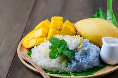 Ahşap arka planda hindistan cevizi sütü ile olgun mango yapışkan pilavı. Geleneksel Tayland Tatlısı.