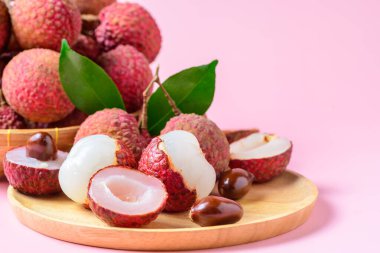 İkiye bölünmüş sulu bir Lychee ve pembe arka planda izole edilmiş ahşap tabakta yapraklar. Tayland meyvesi konsepti