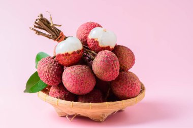 İkiye bölünmüş sulu Lychee ve pembe arka planda izole edilmiş bambu sepetinin üzerinde yapraklar. Tayland meyvesi konsepti
