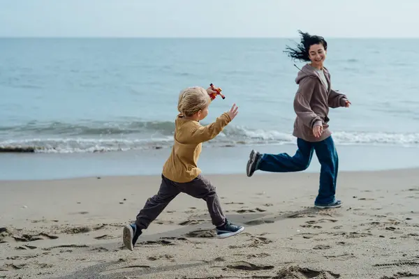 Happy mother running along the beach with her son, enjoying by the sea