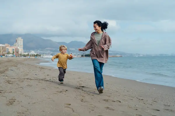 Happy mother running along the beach with her son, enjoying by the sea