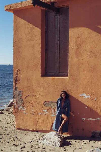 a girl in a denim raincoat poses against the background of a wall. fashion photo shoot on the seashore. stylish shots of a girl model with a beautiful figure.