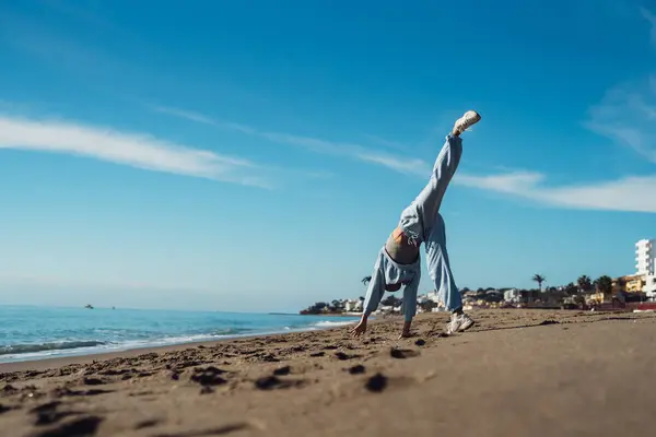 A tanned young woman jumps in a blue suit, a brunette in a tracksuit, an active girl jumps cheerfully on the sea coast. Athletic girl in a tracksuit jumping on the sand