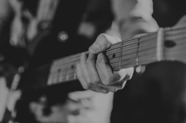 Black and white image of a man playing the guitar, no faces shown , shallow depth of field