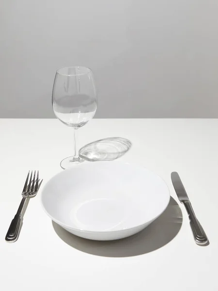 empty white plate with empty red wine glass and fork with knife on white table