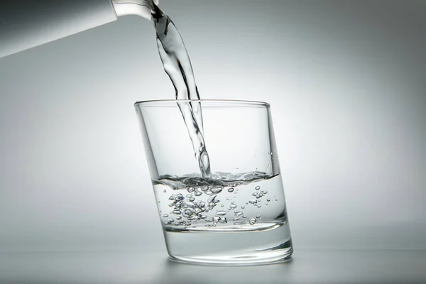 Wasser Ergießt Sich Ein Glas Auf Grauem Hintergrund Nahaufnahme lizenzfreie Stockbilder