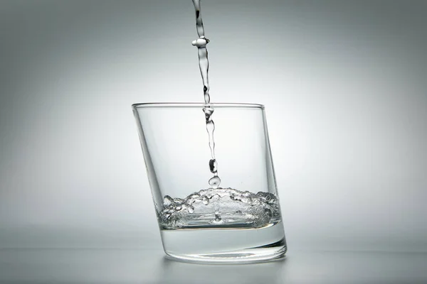 Wasser Ergießt Sich Ein Glas Auf Grauem Hintergrund Nahaufnahme lizenzfreie Stockbilder