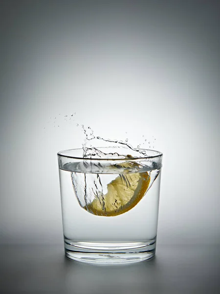 Zitrone Spritzt Ein Glas Wasser Auf Grauem Hintergrund Stockbild