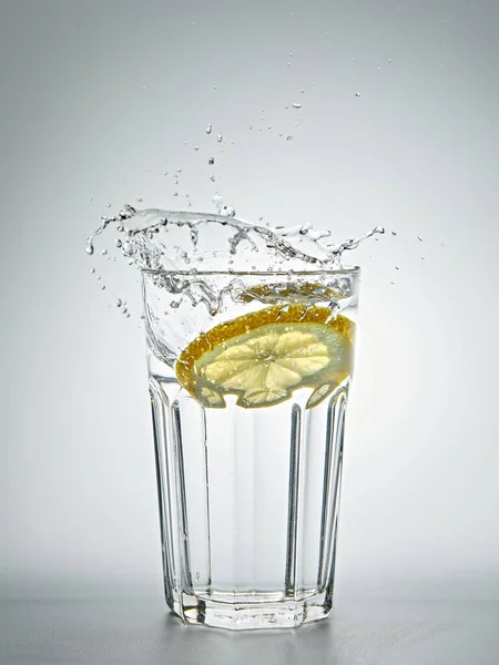 柠檬在灰色背景的一杯水中飞溅 免版税图库照片