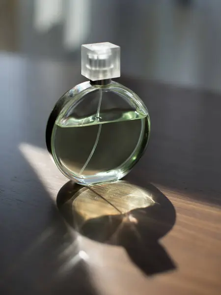 香水瓶放在有阳光和阴影的木制桌子上 图库图片