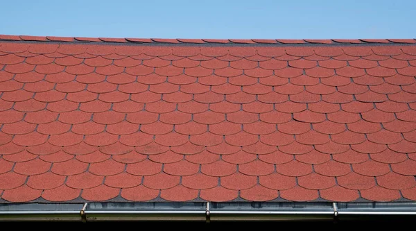 Roof with red bitumen shingles and metal gutter closeup