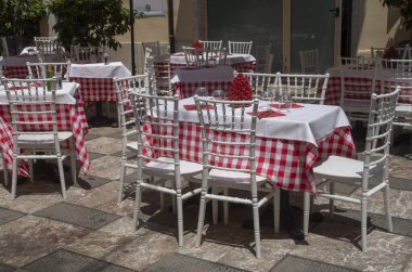Sicilya, İtalya ve Avrupa 'da bir açık hava restoranında kırmızı ve beyaz masa örtüleri ve kırmızı seramik koni ile masalar
