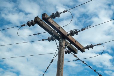 Mavi gökyüzünde çelik halatlarla güçlendirilmiş ahşap elektrik direği.