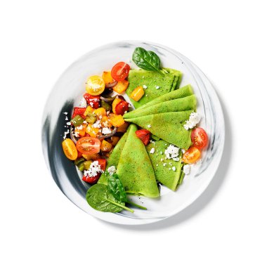 Renkli fırınlanmış biber ve vişneli domatesle servis edilen taze, yeşil ıspanaklı krep. Beyaz arkaplanda izole edilmiş, üst görünüm