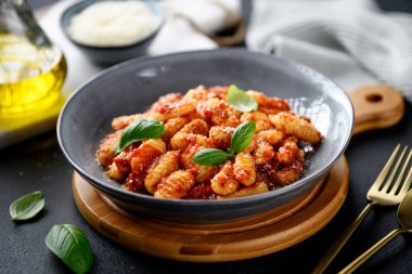 Domates soslu geleneksel İtalyan patatesi gnocchi, parmesan peyniri ve siyah arka planda taze fesleğen yaprakları.