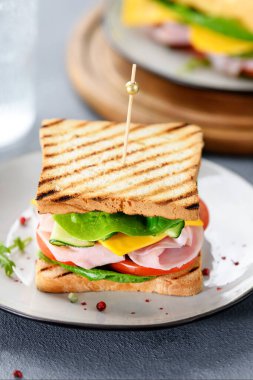 Jambonlu, çedar peynirli, salatalıklı ve domatesli lezzetli bir sandviç.