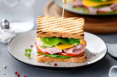 Jambonlu, çedar peynirli, salatalıklı ve domatesli lezzetli bir sandviç.