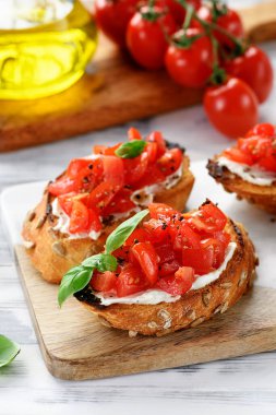 Beyaz ahşap arka planda taze fesleğen yapraklı vişneli domates ve krem peynirli bruschetalar. 