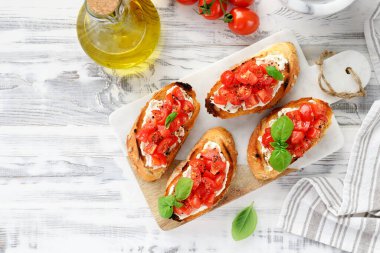 Beyaz ahşap arka planda taze fesleğen yapraklı vişneli domates ve krem peynirli bruschetalar.