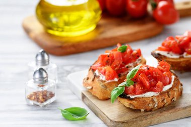 Beyaz ahşap arka planda taze fesleğen yapraklı vişneli domates ve krem peynirli bruschetalar. 