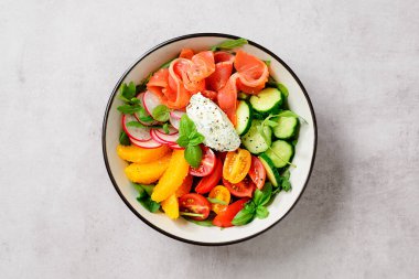 Ispanaklı somon kasesi, roka, kiraz domatesleri, salatalık, portakal dilimleri, turp ve krem peyniri. Lezzetli ve sağlıklı bir yemek konsepti. Açık gri taş arka plan. Üst görünüm.