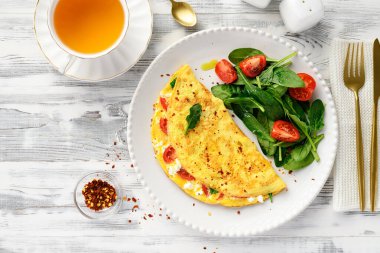 Domatesli omlet ve ricotta peyniri, taze ıspanak yaprakları ve vişneli domateslerle servis edilir. Sağlıklı kahvaltı. Beyaz ahşap arkaplan, üst görünüm