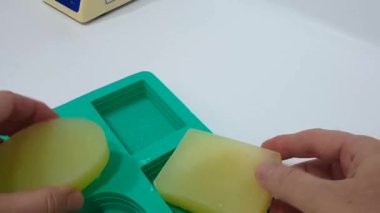 Mavi eldiven giyen ellerin, doğal bir kozmetik laboratuarında silikon kalıp kullanarak yeni yapılmış sabunları öğüttüğü yakın çekim görüntüsü. Bu detaylı görüntüler sanatsal yaratma sürecini vurgular