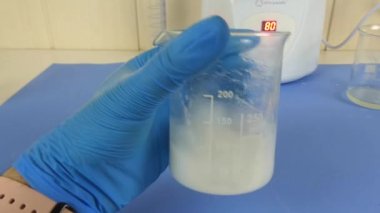 Laboratuvarda hazırlanan kozmetik emülsiyonun makro çekimi. Video, operatörün eldivenli ellerini bir beher kabında karıştırırken yakalıyor. Cilt bakımı, kozmetik ürünleri, laboratuvar süreçleri ve ilaç geliştirme ile ilgili konular için ideal..