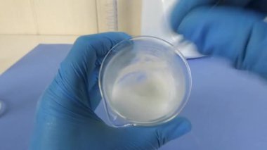 Laboratuvarda hazırlanan kozmetik emülsiyonun makro çekimi. Video, operatörün eldivenli ellerini bir beher kabında karıştırırken yakalıyor. Cilt bakımı, kozmetik ürünleri, laboratuvar süreçleri ve ilaç geliştirme ile ilgili konular için ideal..
